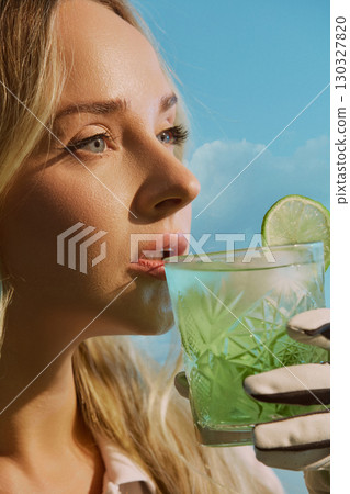Close up of woman drinking cocktail with lime wearing golf glove under blue sky relaxed expression 130327820