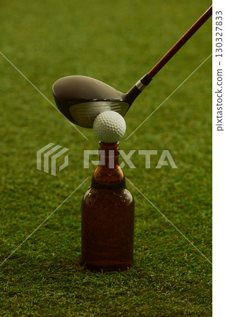 Golf club striking ball balanced on brown beer bottle over green grass bold tension 130327833