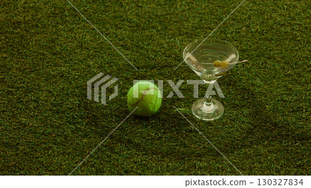 Tennis ball placed beside martini glass with olives on grass surface stylish atmosphere 130327834