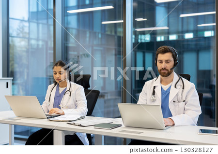 Two doctors collaborating in a modern clinic, wearing headsets and engaging with laptops to provide telehealth services and manage patient data efficiently 130328127