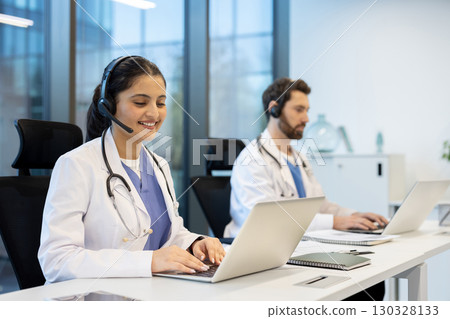 Two doctors are smiling and working on their laptops while wearing headsets in a modern office, providing efficient and accessible healthcare services Two doctors are smiling and working on their laptops while wearing headsets in a modern office, providing efficient and accessible healthcare services 130328133