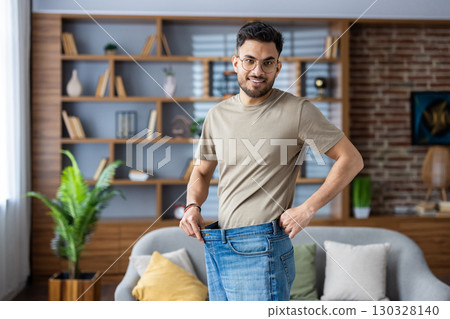 Portrait of a young smiling Indian man standing at home in front of the camera wearing jeans and showing the result of diet, exercise and weight loss. Portrait of a young smiling Indian man standing at home in front of the camera wearing jeans and showing the result of diet, exercise and weight loss. 130328140