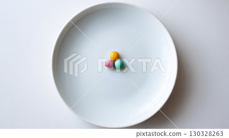 Simple white plate with a single colorful candy piece in the center Simple white plate with a single colorful candy piece in the center 130328263