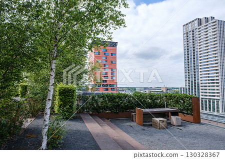 Rooftop garden featuring greenery, wooden benches, and urban skyline, showcasing a blend of nature and modern architecture 130328367