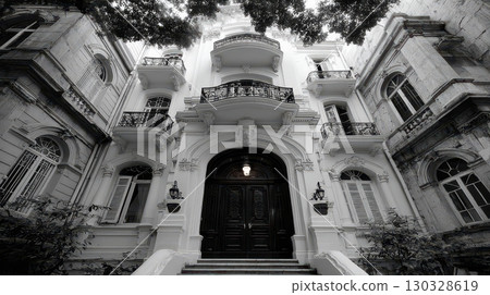 Monochromatic low-angle view of an elegant facade. Ornate balconies and arched windows evoke classical sophistication, highlighting the building's grandeur and historical style 130328619