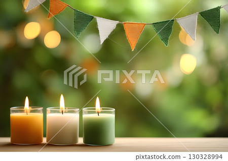 Three candles in saffron, white, and green colors are placed on a wooden surface. A festive bunting with the same colors hangs above, creating a celebratory atmosphere. India, Indian Independence Day. 130328994