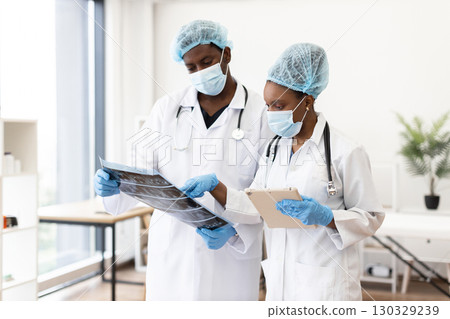 Two adult healthcare professionals, male and female, wearing masks, discussing radiographic tests and notes. Setting highlights teamwork and focus in a sterile medical environment, showcasing hospital 130329239