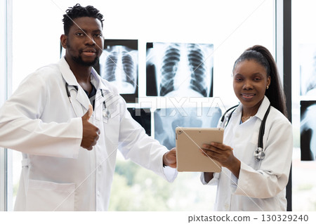 Male and female doctors, adults, consulting at clinic near window analyzing x-rays displayed. Male and female doctors, adults, consulting at clinic near window analyzing x-rays displayed. 130329240
