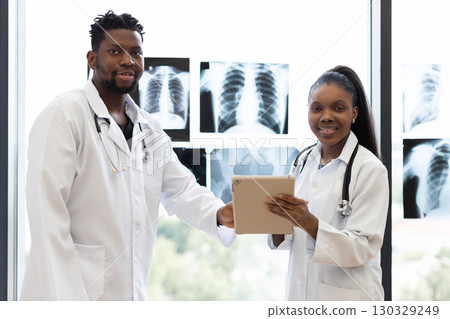 Two medical professionals, male and female, standing in clinic near window discussing x-rays, radiating professionalism and teamwork, symbolizing health care, dedication, expertise. Two medical professionals, male and female, standing in clinic near window discussing x-rays, radiating professionalism and teamwork, symbolizing health care, dedication, expertise. 130329249