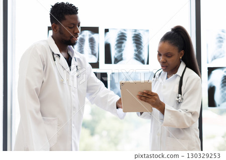 Male and female doctors communicating in medical setting with x-rays displayed near window indoors 130329253