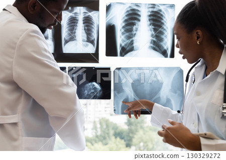 Male and female doctors analyzing x-ray results near clinic window during consultation. They review patient diagnostics to determine findings and treatment options for optimal healthcare solutions. 130329272
