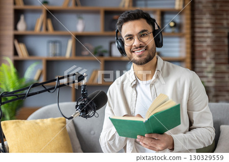 Smiling man wearing headphones recording podcast while reading book. Modern home studio setup with microphone. Engaging in content creation, learning, and sharing information Smiling man wearing headphones recording podcast while reading book. Modern home studio setup with microphone. Engaging in content creation, learning, and sharing information 130329559