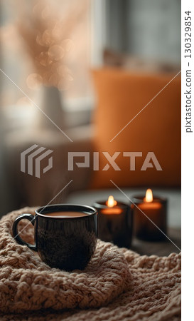 A cozy scene featuring a black mug filled with hot beverage, placed on a knitted blanket. Two lit candles create a warm atmosphere in an autumn setting. A cozy scene featuring a black mug filled with hot beverage, placed on a knitted blanket. Two lit candles create a warm atmosphere in an autumn setting. 130329854