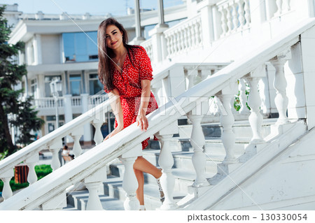 Stylish girl in summer outfit: , red dress, white bag walk on old city streets 130330054
