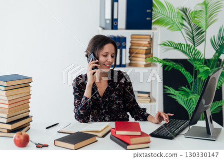 Woman working in an office browsing her phone while sitting in front of a computer 130330147