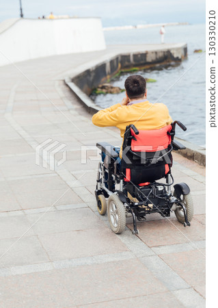 Rear view of disabled Caucasian man sitting with arms up on wheelchair at beach. Rear view of disabled Caucasian man sitting with arms up on wheelchair at beach. 130330210