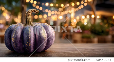 A decorative purple pumpkin sits on a wooden table. Soft bokeh lights create a warm, festive atmosphere, perfect for autumn and Halloween parties. 130330285