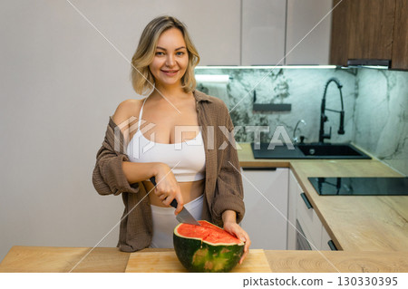 A sensual woman enjoys a slice of juicy watermelon in a modern kitchen. Confident, playful, and radiant, she savors the moment with a hint of summer flirtation. A sensual woman enjoys a slice of juicy watermelon in a modern kitchen. Confident, playful, and radiant, she savors the moment with a hint of summer flirtation. 130330395