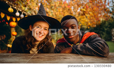 A young Caucasian woman with long brown hair wears a witch hat. A young African man with short hair wears a cape. They smile together in a festive Halloween setting. A young Caucasian woman with long brown hair wears a witch hat. A young African man with short hair wears a cape. They smile together in a festive Halloween setting. 130330480