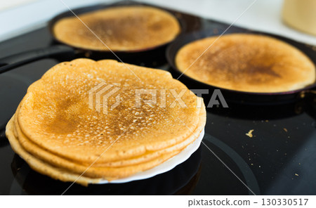 freshly baked hot cereal pancakes on plate and pans during cooking 130330517