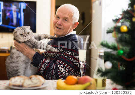 Older man with gray cat sitting at home table at Christmas 130330522