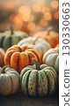 A collection of various pumpkins in different colors and sizes, including orange, white, and green. The scene is warm and festive, suitable for Thanksgiving and Halloween themes. 130330663