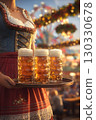 A young Caucasian woman in traditional Bavarian attire holds a tray with three large beer mugs at an Oktoberfest celebration. Colorful decorations fill the background. 130330678