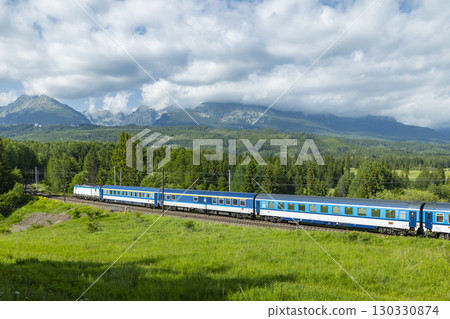 Train passing through green fields with High Tatras mountains in background, Slovakia 130330874