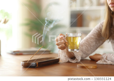 Woman hand holding tea cup beside incense stick burning 130331124