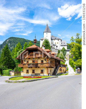 Mauterndorf Castle stands majestically against the backdrop of the Austrian Alps. A charming wooden building features colorful flowers, showcasing the region's beauty and rich history. 130331238