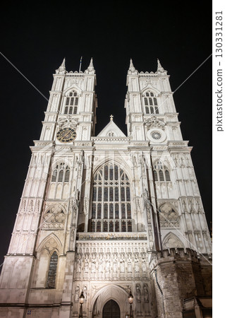 Westminster Abbey stands majestically under the night sky, showcasing its gothic architecture. The illuminated facade highlights intricate details, captivating visitors in London, England. 130331281