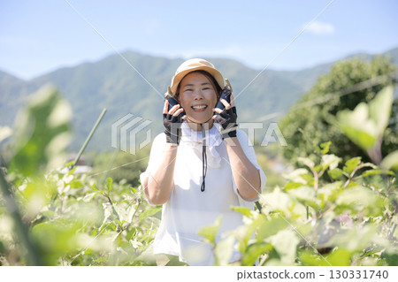 Woman harvesting vegetables in the field. Image of a farmer or agricultural worker. Close-up of a smiling woman looking at the camera. 130331740