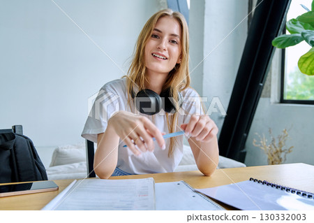 Webcam portrait female college student, sitting at home at the table with textbooks Webcam portrait female college student, sitting at home at the table with textbooks 130332003