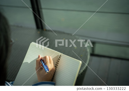 Close-up of woman's hand writing in notebook outdoors. Self-reflection, goal setting, journaling habit, and mindful planning. Creativity, life planning, and focus on personal growth. Mindful practice. 130333222