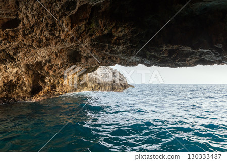 A picturesque sea cave frames a view of tranquil blue waters and an open sky 130333487