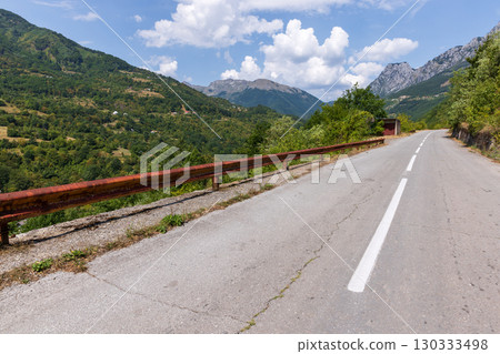 A tranquil mountain road with a railing overlooks lush forested hills A tranquil mountain road with a railing overlooks lush forested hills 130333498