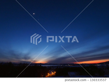 日落後，黃昏時分，月亮在深藍色的天空中閃耀著白光，地平線被餘暉染成橙色，形成一幅引人注目的美麗景象。 130333537