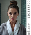 Woman in bathrobe in the bathroom looks at camera with surprised expression on her face 130333890