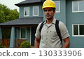 Man in yellow helmet standing in front of the house. He's wearing uniform and he's construction 130333906