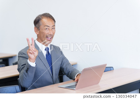 Senior businessman using a computer and making a peace sign 130334047