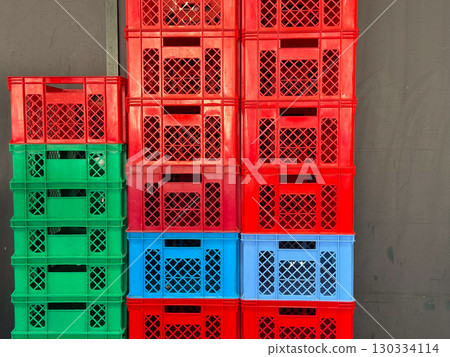 Stacked plastic crates in red, green and blue arranged against a wall creating industrial pattern. Storage, logistics and retail packaging symbolizing distribution, economy and commerce. Stacked plastic crates in red, green and blue arranged against a wall creating industrial pattern. Storage, logistics and retail packaging symbolizing distribution, economy and commerce. 130334114