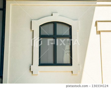 Window with decorative frame design placed on a light-colored building facade in sunlight. Architecture, urban housing and construction detail representing geometry, symmetry and modern residential Window with decorative frame design placed on a light-colored building facade in sunlight. Architecture, urban housing and construction detail representing geometry, symmetry and modern residential 130334124