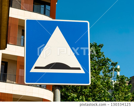 Traffic sign indicating speed bump displayed on a blue board along an urban street. Safety, regulation and transportation infrastructure highlighting prevention, mobility control and caution for Traffic sign indicating speed bump displayed on a blue board along an urban street. Safety, regulation and transportation infrastructure highlighting prevention, mobility control and caution for 130334125