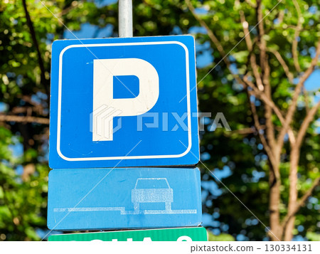 Blue parking sign with white letter P displayed on a metal pole in urban area. Transportation, regulation and public infrastructure ensuring vehicle orientation, law and city mobility. Blue parking sign with white letter P displayed on a metal pole in urban area. Transportation, regulation and public infrastructure ensuring vehicle orientation, law and city mobility. 130334131