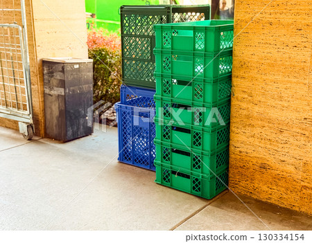 Plastic crates stacked in green and blue colors near a market wall for storage and logistics. Commerce, distribution and retail supply organization for product handling and urban trade. 130334154