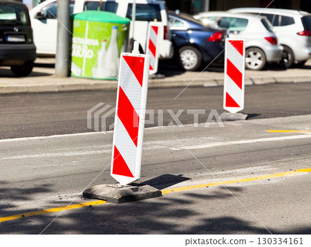 Reflective red-and-white striped roadwork bollards placed in a city street to guide traffic around construction. Reflective red-and-white striped roadwork bollards placed in a city street to guide traffic around construction. 130334161