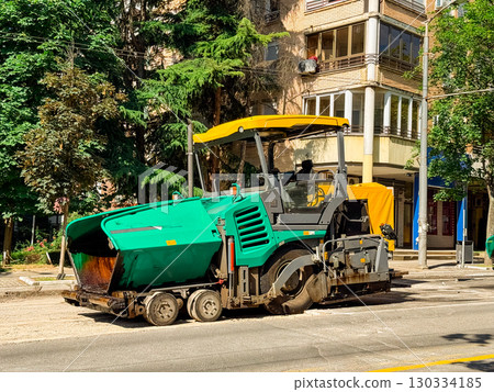 Road paver working on a street. Construction, urban infrastructure, and industrial machinery in city development. 130334185