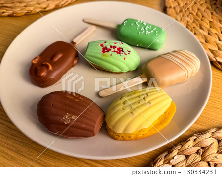 Assorted desserts on a plate, colorful cakes and popsicles. Modern food styling. Concept of variety, sweets, aesthetics of food. Assorted desserts on a plate, colorful cakes and popsicles. Modern food styling. Concept of variety, sweets, aesthetics of food. 130334231