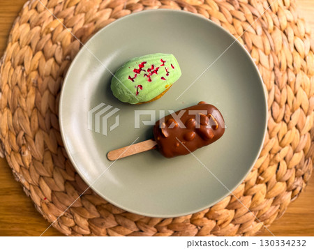 Two desserts on a plate: chocolate popsicle and green cake. Modern presentation of sweets. Food, pleasure, gastronomy concept 130334232