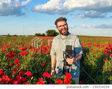 Smiling man with retro camera in blooming poppy field. Joy, creativity and passion for photography in nature. Smiling man with retro camera in blooming poppy field. Joy, creativity and passion for photography in nature. 130334238